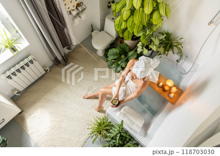 A young, beautiful woman sits on the edge of a bubble bath and applies moisturizer to her skin. 118703030