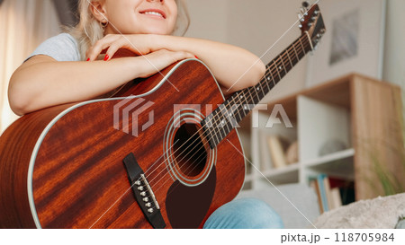 Music composer. Romantic woman. Home playing. Smiling female player holding guitar on knees dreaming about new song sitting sofa in light room interior. 118705984