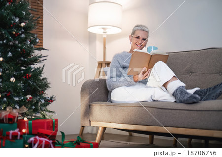 Peaceful Christmas Evening Elderly Woman Relaxes with Book by the Decorated Tree 118706756