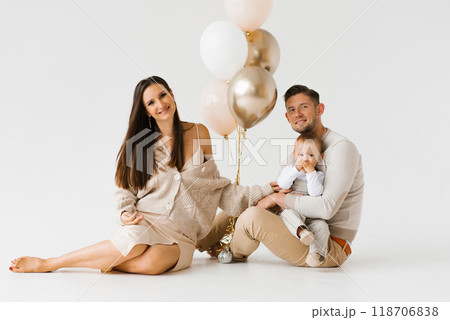 Happy family with a one year old birthday boy are sitting on the floor next to balloons Happy family with a one year old birthday boy are sitting on the floor next to balloons 118706838