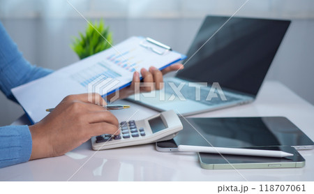 Businesswoman hand working with finances about cost and calculator and laptop with tablet on desk at office in morning light, Business accounting concept, Calculating or checking balance. 118707061
