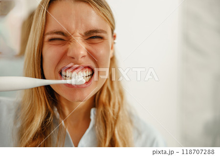 A young woman happily brushing her teeth with an electric toothbrush in her bathroom A young woman happily brushing her teeth with an electric toothbrush in her bathroom 118707288