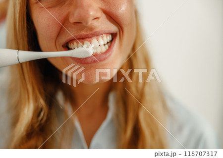 A woman in her morning routine brushing her teeth with an electric toothbrush for hygiene A woman in her morning routine brushing her teeth with an electric toothbrush for hygiene 118707317