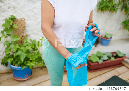 Woman preparing for outdoor workout with resistance band in a garden setting, focusing on fitness and wellness activities amid lush green plants Woman preparing for outdoor workout with resistance band in a garden setting, focusing on fitness and wellness activities amid lush green plants 118709247