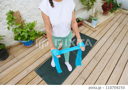 Woman practicing resistance band workout on wooden deck in outdoor garden setting 118709250