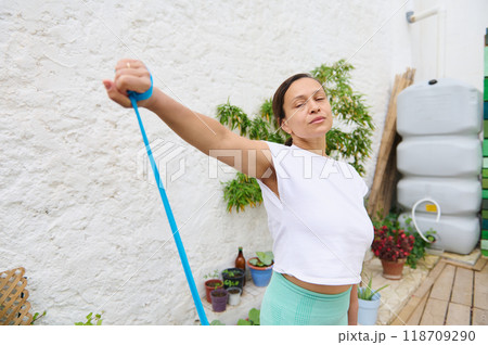 Woman exercising outdoors with resistance band in peaceful garden setting promoting a healthy lifestyle and fitness routine Woman exercising outdoors with resistance band in peaceful garden setting promoting a healthy lifestyle and fitness routine 118709290