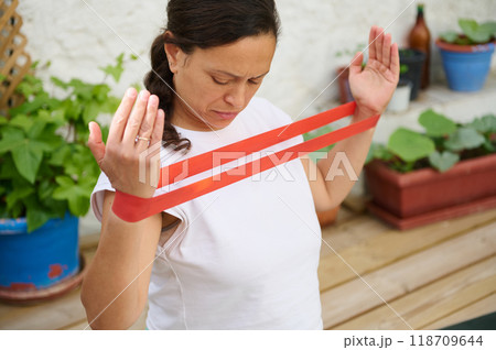 Woman exercising with resistance band in a garden setting, focusing on upper body strength and home fitness. Woman exercising with resistance band in a garden setting, focusing on upper body strength and home fitness. 118709644