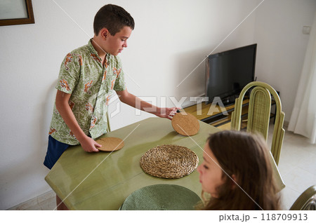 Young boy and girl preparing dining table with placemats in a cozy home setting Young boy and girl preparing dining table with placemats in a cozy home setting 118709913