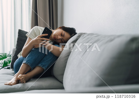 Unhappy lonely depressed woman is sitting on the couch and using a phone. 118710316