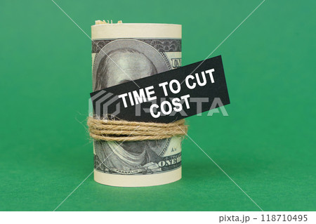 On a green surface, rolled dollars with a black sign that says - Time to cut cost 118710495