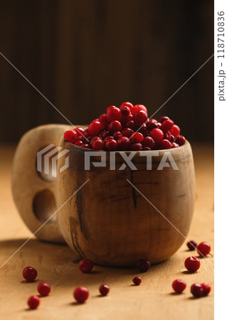 A wooden finnish kuksa cup full of forest ripe lingonberries on a wooden background, close-up A wooden finnish kuksa cup full of forest ripe lingonberries on a wooden background, close-up 118710836