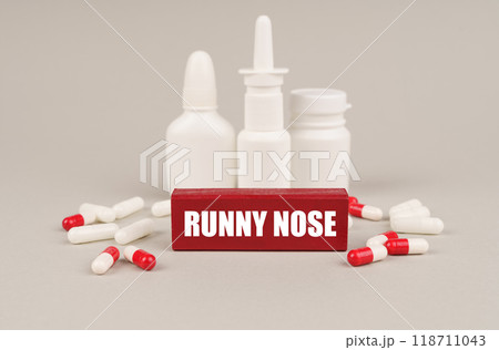 On a gray surface are pills, white jars and a red wooden block with the inscription - Runny nose 118711043