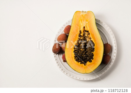 Half of a beautiful juicy ripe papaya and lychee on a white plate on a white table Half of a beautiful juicy ripe papaya and lychee on a white plate on a white table 118712128