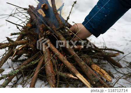 In the forest, a man makes a fire by setting dry firewood on fire to keep warm. A man is engaged in survival in extreme conditions in the forest in winter. Making a fire to keep warm in winter. In the forest, a man makes a fire by setting dry firewood on fire to keep warm. A man is engaged in survival in extreme conditions in the forest in winter. Making a fire to keep warm in winter. 118712714