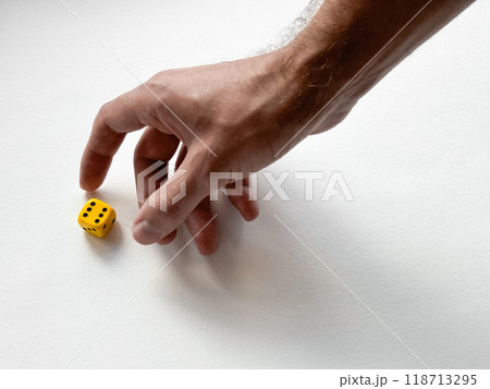 Hand reaching for yellow dice on white background symbolizing chance and decision-making Hand reaching for yellow dice on white background symbolizing chance and decision-making 118713295