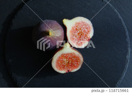 Purple figs on a black stone plate. Photo, background with fresh, juicy, ripe tropical fruits. Suitable for depicting vegetarian and raw, healthy food, harvest. Symbol of abundance and enlightenment. 118715661