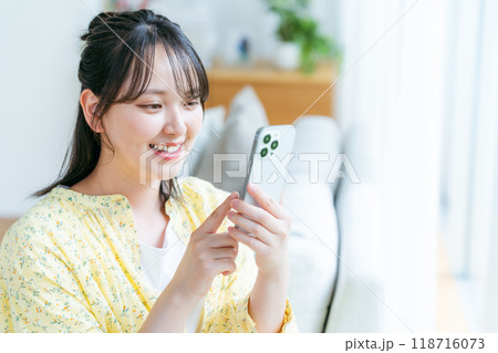 部屋でスマホを操作する若い女性 118716073