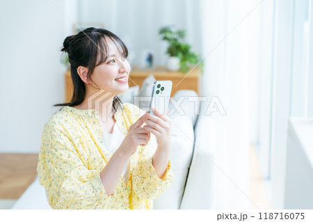 部屋でスマホを操作する若い女性 118716075