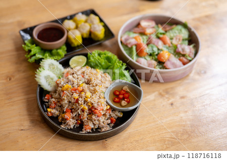 A wooden dining table featuring a plate of fried rice, a salad bowl, and a plate of steamed dumpling A wooden dining table featuring a plate of fried rice, a salad bowl, and a plate of steamed dumpling 118716118