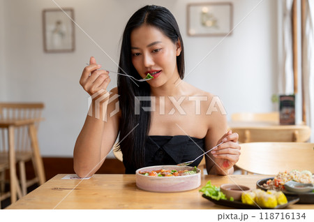 A gorgeous Asian woman is enjoying a healthy salad at a restaurant during lunchtime. A gorgeous Asian woman is enjoying a healthy salad at a restaurant during lunchtime. 118716134