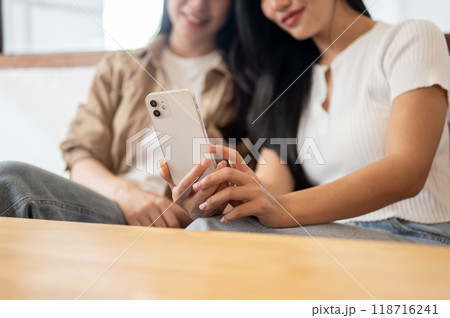 Two happy female friends enjoying a conversation while watching something on a smartphone together. 118716241
