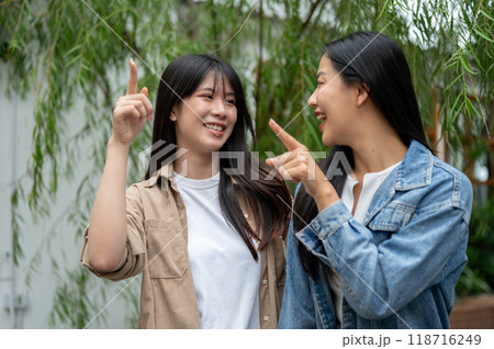 Two attractive Asian female friends are enjoying the view in a lush home garden. Two attractive Asian female friends are enjoying the view in a lush home garden. 118716249