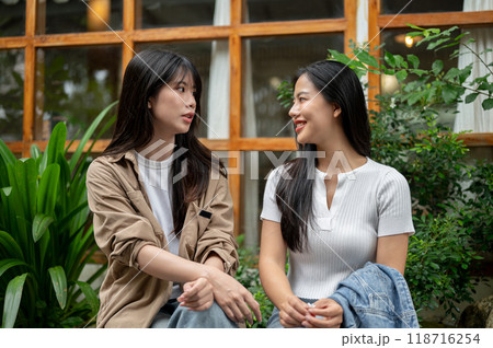 Two young Asian female friends are engaged in conversation in a beautiful garden. Two young Asian female friends are engaged in conversation in a beautiful garden. 118716254