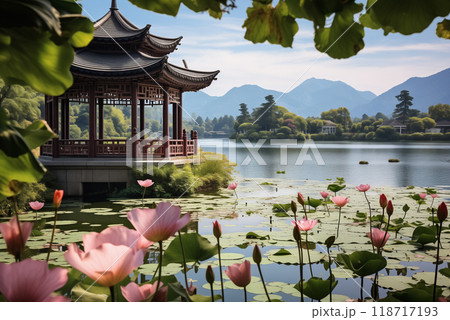 Chinese gazebo in the distance on a lake with blooming pink lotuses, mountains in the background 118717193