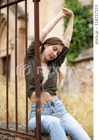 Portrait of seductive woman near forged fence against background of an abandoned building Portrait of seductive woman near forged fence against background of an abandoned building 118717513
