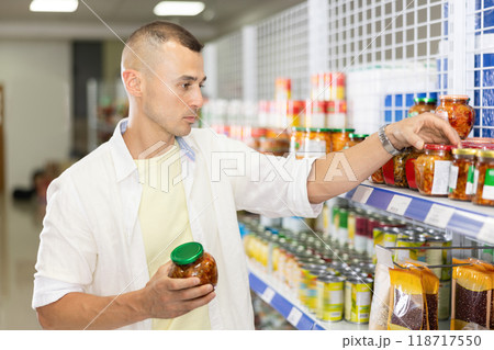 Young man choosing canned pickled vegetables in Asian store Young man choosing canned pickled vegetables in Asian store 118717550