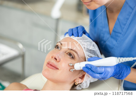 Adult woman cosmetologist doing microcurrent procedure to young woman 118717568
