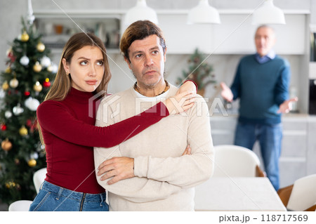 Sad couple listens to their elderly father scream and swear while celebrating Christmas. Family quarrel Sad couple listens to their elderly father scream and swear while celebrating Christmas. Family quarrel 118717569