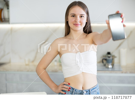 In kitchen, smiling girl in casual clothes shows blank smartphone screen close-up In kitchen, smiling girl in casual clothes shows blank smartphone screen close-up 118717877