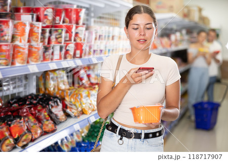 Girl scanning QR code on cup of instant noodles with smartphone in store 118717907