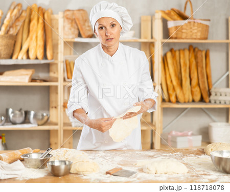 Professional female baker preparing pizza dough in bakery 118718078