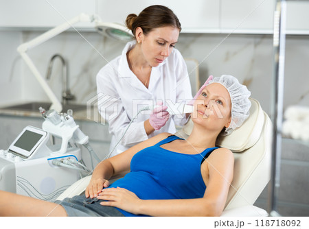 Young beautician doing procedure for face lifting and Soften skin keratin, deep clear skin dirt of adult woman laying in salon. Hardware cosmetology Young beautician doing procedure for face lifting and Soften skin keratin, deep clear skin dirt of adult woman laying in salon. Hardware cosmetology 118718092