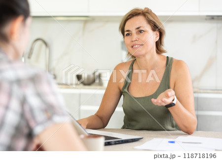 Two middle-aged women having business conversation in the kitchen Two middle-aged women having business conversation in the kitchen 118718196