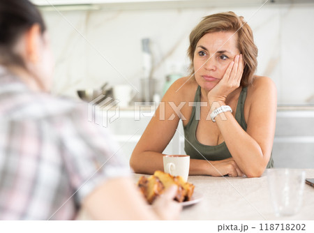 Two women friends share problems with each other in home kitchen Two women friends share problems with each other in home kitchen 118718202