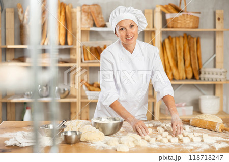 Female baker preparing croissant dough - kneading, rolling and cutting dough on table in bakery Female baker preparing croissant dough - kneading, rolling and cutting dough on table in bakery 118718247