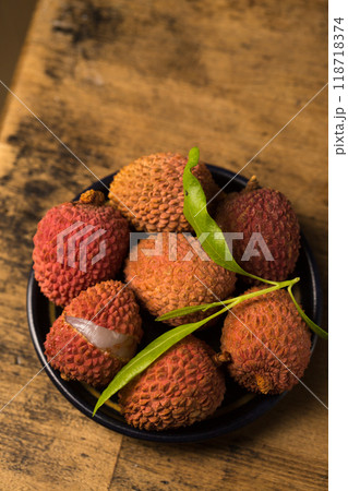 Small ripe tropical lychee berries on a black plate on a wooden background Small ripe tropical lychee berries on a black plate on a wooden background 118718374