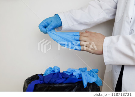 Doctor throws disposable gloves into trash bin. Medical waste disposal and treatment. Close up of medical worker's hands after work in hospital. 118718721