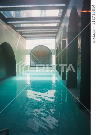 Elegant indoor swimming pool in a high-end luxury hotel, featuring arched openings, skylights, and serene turquoise water illuminated by natural light. 118719814