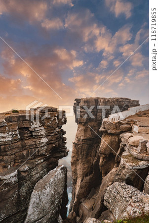 Stunning sunset over Cabo Carvoeiro in Peniche, Portugal, highlighting rugged cliffs, a narrow chasm, and the faintly visible Atlantic Ocean. 118719855