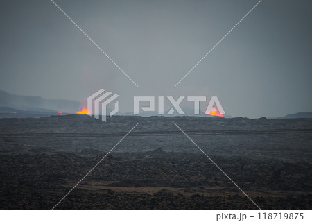 A powerful scene of Iceland's volcanic activity featuring dark rocky terrain, bright orange lava, and smoke under an overcast sky. Captures nature's raw power. A powerful scene of Iceland's volcanic activity featuring dark rocky terrain, bright orange lava, and smoke under an overcast sky. Captures nature's raw power. 118719875