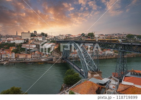 The iconic Dom Luis I Bridge spans the Douro River in Porto, Portugal, with historic buildings and terracotta rooftops under a dramatic sunset sky. The iconic Dom Luis I Bridge spans the Douro River in Porto, Portugal, with historic buildings and terracotta rooftops under a dramatic sunset sky. 118719899