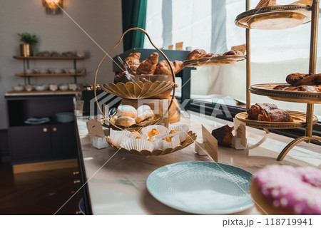 Elegant display of croissants and baked goods on a two-tiered golden tray in a well-lit, sophisticated hotel dining area with marble countertops. Elegant display of croissants and baked goods on a two-tiered golden tray in a well-lit, sophisticated hotel dining area with marble countertops. 118719941