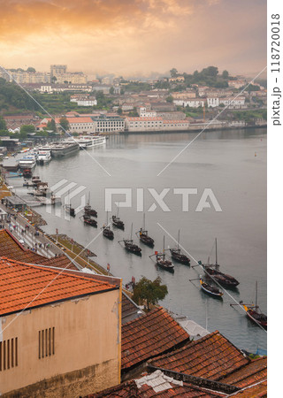 A picturesque scene of the Douro River in Porto, Portugal, featuring traditional Rabelo boats, terracotta rooftops, historic buildings, and a golden sky at sunrise. A picturesque scene of the Douro River in Porto, Portugal, featuring traditional Rabelo boats, terracotta rooftops, historic buildings, and a golden sky at sunrise. 118720018