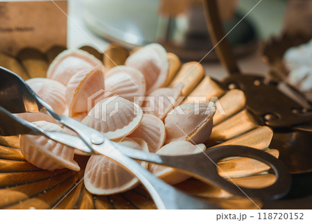 Close-up of a golden tray filled with delicate, shell-shaped confections in a high-end hotel or restaurant. Silver tongs are placed on the tray, ready for use. 118720152
