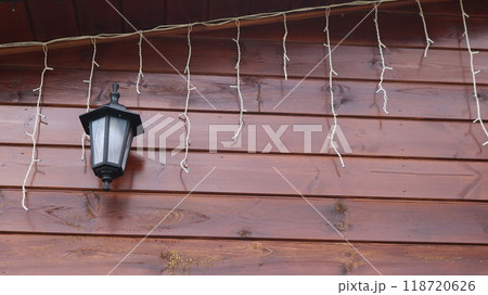 wall lamp in black case with white frosted glass and light garland hanging on wooden ceramic wall under roof of house made of horizontal boards in off position wall lamp in black case with white frosted glass and light garland hanging on wooden ceramic wall under roof of house made of horizontal boards in off position 118720626
