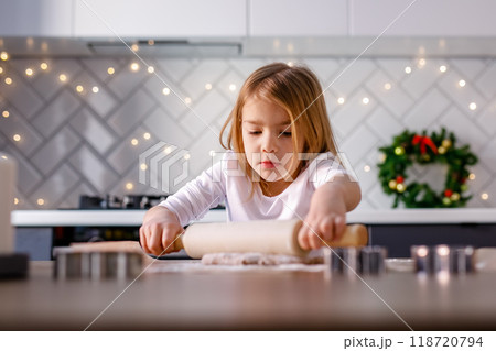A girl is rolling out dough for gingerbread cookies in the kitchen, embracing the Christmas spirit 118720794